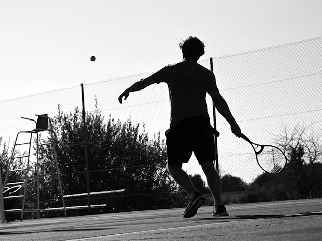 Beginner tennis player receiving instruction from coach on outdoor court, showing the welcoming nature of tennis for newcomers